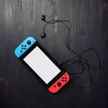 a picture of a nintendo switch console with bright joy-con controllers and headphones on vintage wood table background