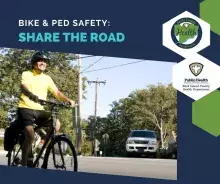 Bike and pedestrian safety awareness banner with text “Bike & Ped Safety: Share the Road,” featuring a smiling adult cyclist wearing a helmet and yellow shirt riding a bicycle on a suburban street, with a car approaching in the background, trees and utility poles visible, and official logos for Scott County Health Department and Rock Island County Public Health Department on a blue and green graphic layout.