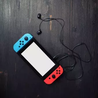 a picture of a nintendo switch console with bright joy-con controllers and headphones on vintage wood table background