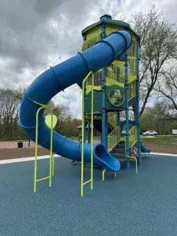 The photo depicts a brightly colored playground structure with a tall slide tower and interactive features.