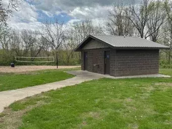 The photo depicts a brown block restroom and sand volleyball court.