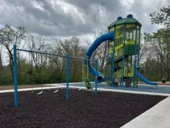 The photo depicts the playground equipment at High Meadows Shelter which includes a bright blue and green slide tower and slides.