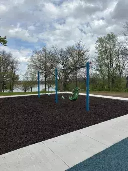 A playground swing set with three standard swings and one accessible swing, all positioned over a rubber mulch safety surface.