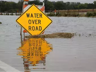 Water Over Road warning sign surrounded by flood waters.