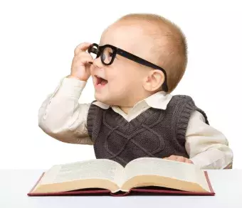 This is a baby wearing glasses and holding a bookl.