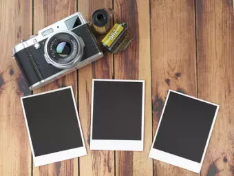 Retro camera, empty photo frames pictures and film canisterrs on wood table.