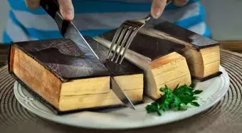 a cake that looks like a book but you can eat and a person cutting it with a knife and fork