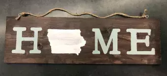 A wooden sign with the word "home" painted on; an outline of the state of Iowa is in place of the "o"