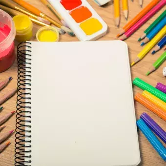 Notebook, paints, colored pencils, and other art supplies on a wooden background