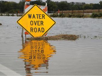 Water Over Road warning sign surrounded by flood waters.