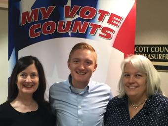 Three voters posing for a selfie in front of the my vote counts poster.