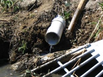 Effluent pipe with a stream of water dripping it a watery ditch.