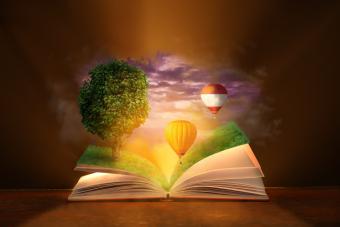 Open magic book with flying hot air balloons and growing tree on dark background