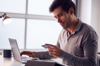 This is a man holding a credit card while sitting at a laptop computer. 