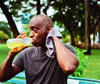 Picture of a man who is sitting in the park, wiping off sweat and drinking a cool drink