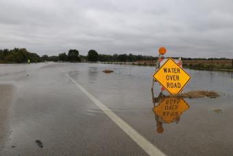 "Water Over Road" sign on roadway submerged in water.