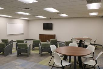 Chairs and tables facing a white board and TV in the new program area.