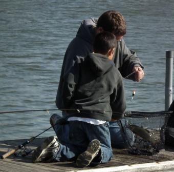 Picture of a grown man and child on a boat dock with trout in a fishing net.