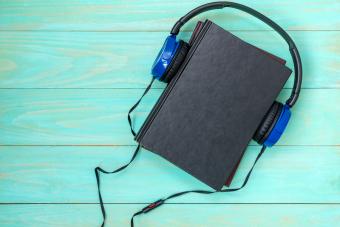 Headphones put over hardback book with empty cover on blue wooden background