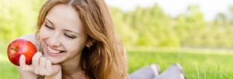 Woman laying in the grass, smiling at an apple.  