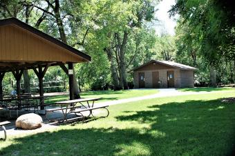 Side view of picnic shelter with sand volleyball and modern restroom in background.