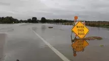 "Water Over Road" sign on roadway submerged in water.
