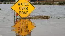 Water Over Road warning sign surrounded by flood waters.