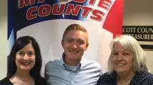 Three voters posing for a selfie in front of the my vote counts poster.