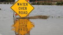 Water Over Road warning sign surrounded by flood waters.