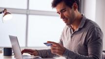 This is a man holding a credit card while sitting at a laptop computer. 