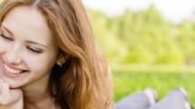 Woman laying in the grass, smiling at an apple.  