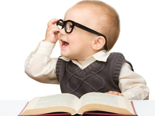 This is a baby wearing glasses and holding a bookl.