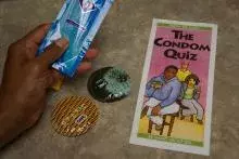 a hand holding a Condom Quiz brochure next to two condom wrappers. 