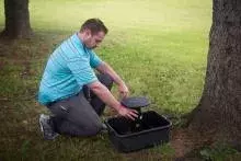 Environmental staff member checking a mosquito trap near a tree in a park. 